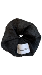Black textured scrunchie with a white label on a white background